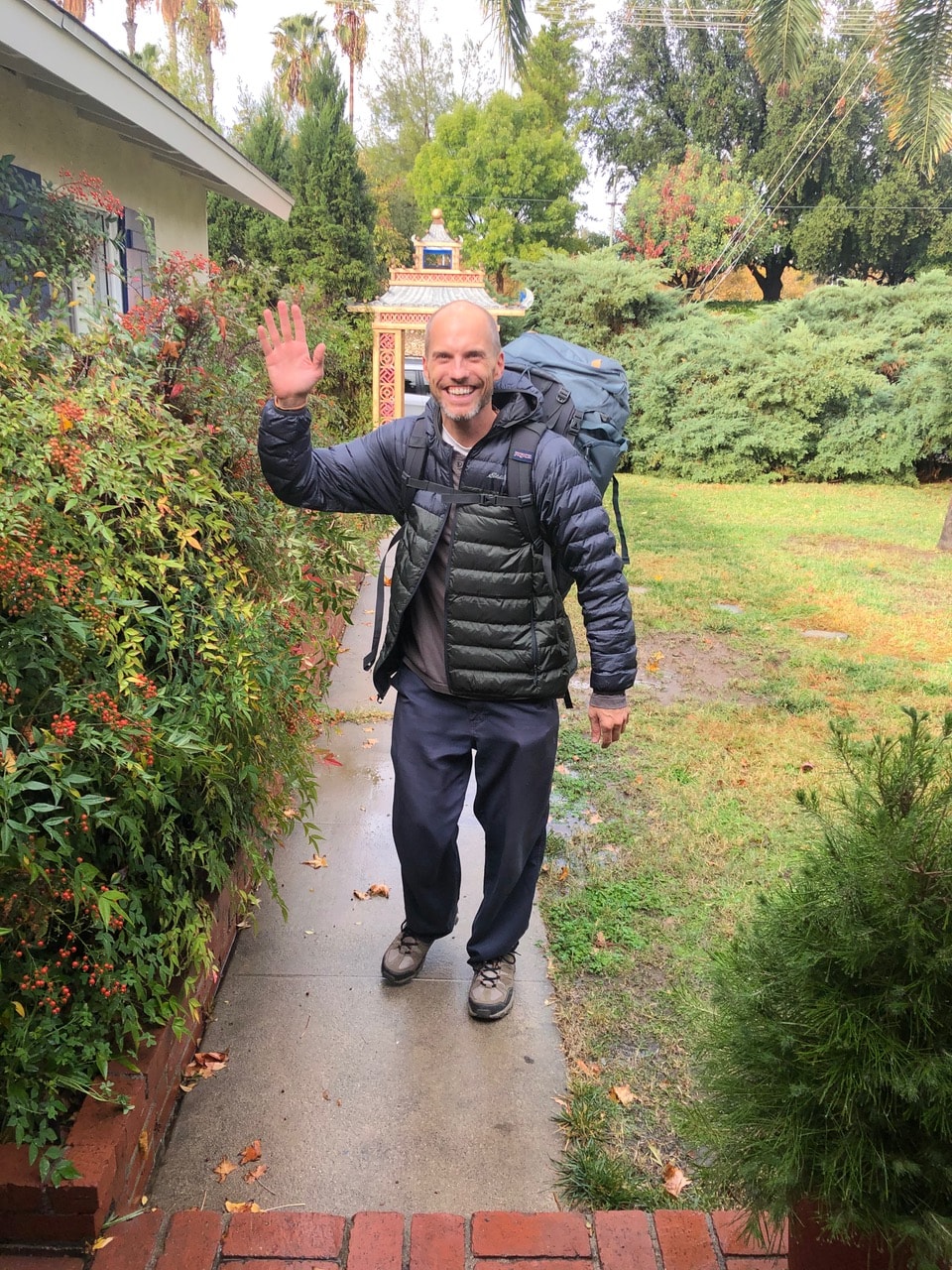 A smiling visitor walking through a lush garden with a backpack
